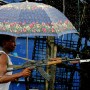 A Liberian government gunman holding an umbrella, a rifle and a crutch for the bullet wound in his leg fires over the 'Old Bridge' in  torrential rains, Monrovia 28 July 2003. LURD(Liberians United for Reconciliation and Democracy) rebels drove government forces back over the bridge last night leaving the government forces on the Monrovia side of the bridge defending the city.
